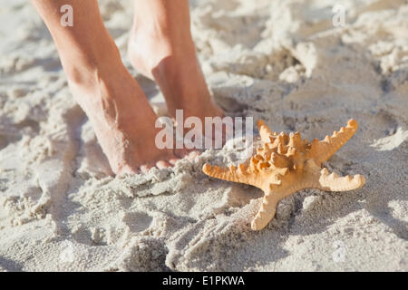 Woman standing beside starfish on the beach Stock Photo