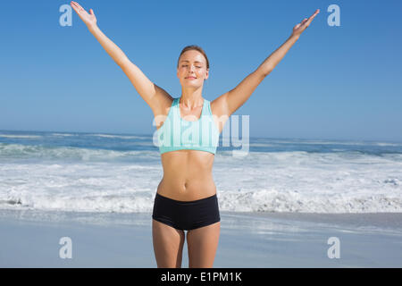 Fit woman standing on the beach with arms up Stock Photo