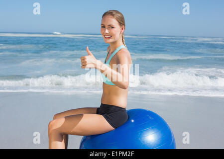 Fit woman sitting on exercise ball at the beach smiling at camera Stock Photo