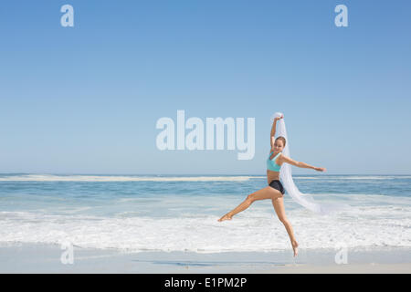 Fit woman jumping gracefully on the beach with scarf Stock Photo