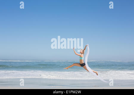 Fit woman jumping gracefully on the beach with scarf Stock Photo