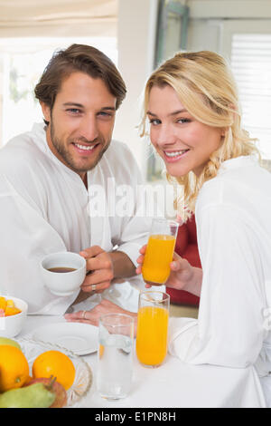 Cute couple in bathrobes having breakfast together smiling at camera Stock Photo