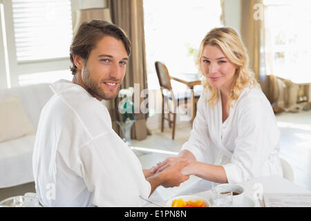 Cute couple in bathrobes having breakfast together holding hands Stock Photo