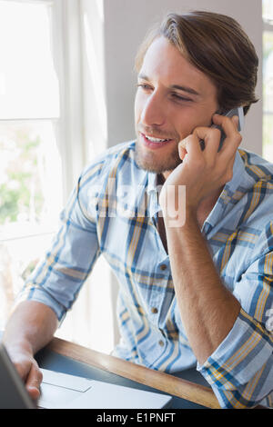 Smiling casual man using laptop and talking on smartphone Stock Photo