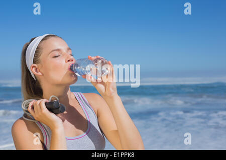 Sporty blonde standing on the beach with bottle and skipping rope Stock Photo