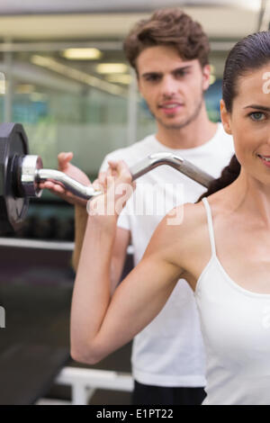 Fit smiling woman lifting barbell with her trainer Stock Photo