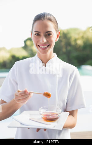 Smiling beauty therapist looking at camera holding plate with honey Stock Photo