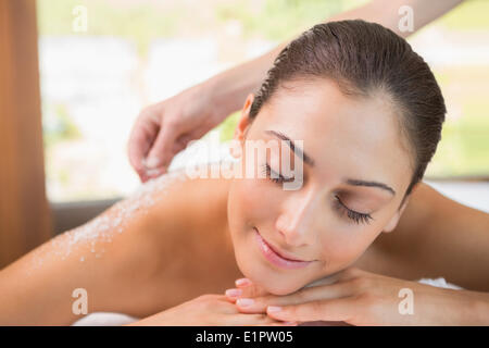 Beauty therapist pouring salt scrub on smiling womans back Stock Photo