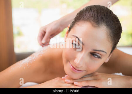 Beauty therapist pouring salt scrub on smiling womans back Stock Photo