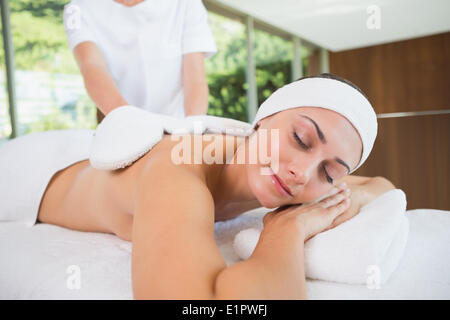 Beauty therapist rubbing smiling womans back with heated mitts Stock Photo