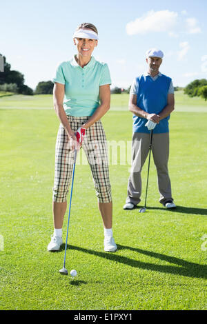 Smiling lady golfer teeing off for the day watched by partner Stock Photo