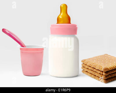 Baby's bottle of milk and an empty yoghurt pot and rich tea biscuits Stock Photo