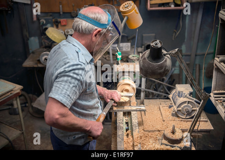 The aged man grinds out wood wares on a lathe in his joinery workshop. Stock Photo