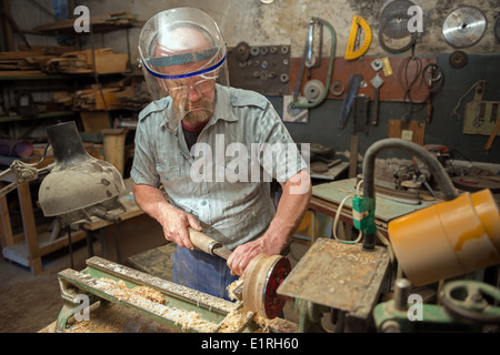 The aged man grinds out wood wares on a lathe in his joinery workshop. Stock Photo