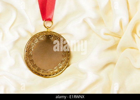 A rugged gold medal setup majestically against a cream colored silk cloth. Stock Photo