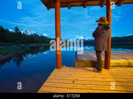 Woman looking at mountains on dock of Maligne Lake boathouse at dusk, Jasper National Park, Alberta, Canada.