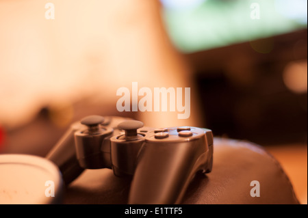games controller sitting on a sofa arm with football game playing in background Stock Photo