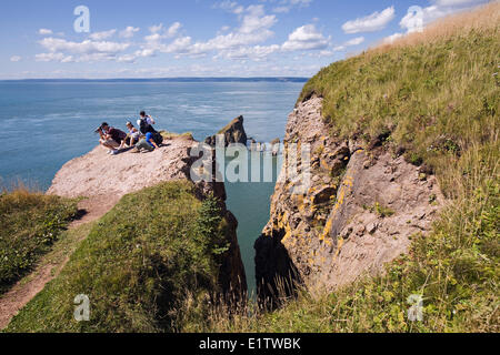 Hikers view the rock formations from atop cliffs at the end of the Cape Split hiking trail along Nova Scotia's Bay of Fundy coas Stock Photo