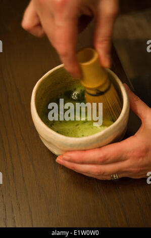 Woman preparating Japanese matcha tea in a cup with a whisk Stock Photo