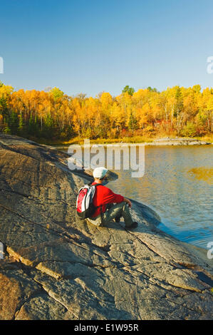 Hiker relaxes on precambrian shield rock along the Winnipeg River, near Seven Sisters, Manitoba, Canada Stock Photo