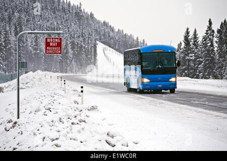 Wrong way sign and tour bus on Trans-Canada Highway in winter conditions near Lake Louise, Banff, Albert, Canada