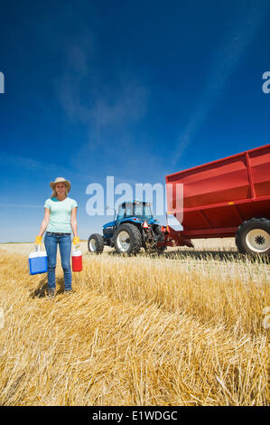 a farm girl standing in oat stubble in front of a tractor and grain wagon during the harvest, near Dugald, Manitoba, Canada