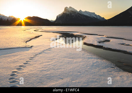 Sun rising beside Mount Rundle reflecting on ice on snow covered Vermilion Lakes in winter in Banff National Park Alberta Stock Photo