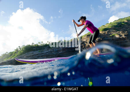 A woman paddles on her stand-up paddleboard off the cliffs of Honolulu, Oahu, Hawaii Stock Photo