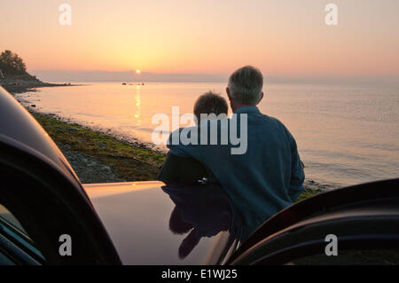 An older couple watch the sunrise at Point Holmes Beach from their 1939 Ford. Courtenay, BC Stock Photo