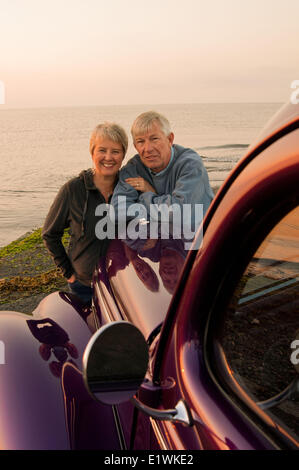 An older couple watch the sunrise at Point Holmes Beach from their 1939 Ford. Courtenay, BC Stock Photo