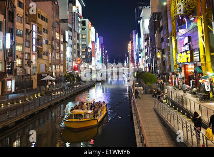 Tour boat cruising along the famous Dotombori canal in Osaka, Japan, are numerous restaurants and cafes, as well as a 4-story di Stock Photo