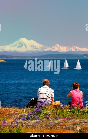 A couple watch laser sailboats racing off Cattle Point in Oak Bay in Victoria, BC. Stock Photo