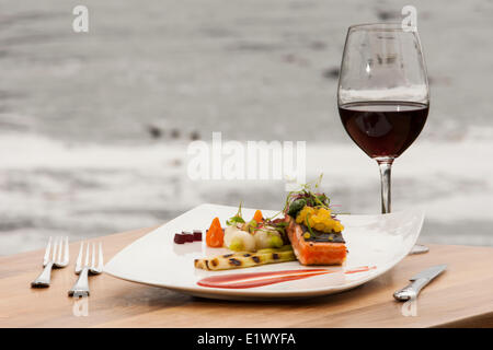 A single serving Salmon main course with accompanying red wine served up fresh at the Black Rock Resort in Ucluelet.  Ucluelet Stock Photo