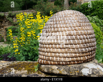Skep beehive, a traditional form used for over 2000 years perched on a wall in an English garden. Stock Photo