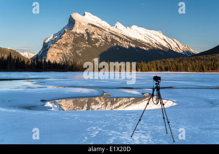 Camera on a tripod facing Mount Rundle on frozen Vermilion Lakes at sunset in winter, Banff National Park, Alberta, Canada Stock Photo