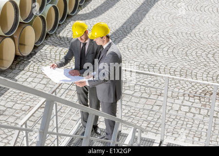Full length of young male engineers examining blueprint on stairway Stock Photo