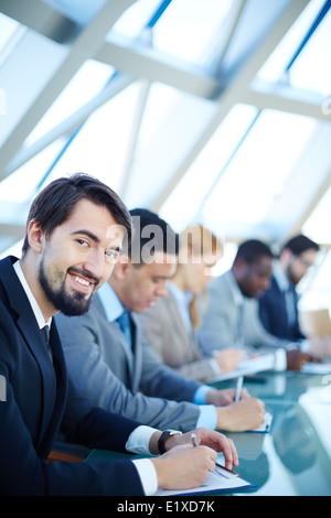 Row of business people listening to presentation at seminar with smiling young man on foreground Stock Photo