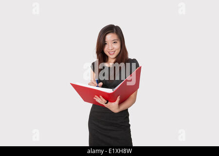 Portrait of beautiful young businesswoman writing notes in folder over white background Stock Photo
