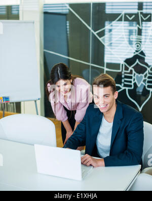 Portrait of smiling young businessman with female colleague using laptop at table in office Stock Photo