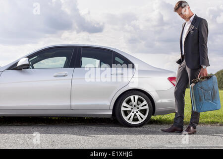 Full length of sad young businessman carrying gas can by broken down car at countryside Stock Photo