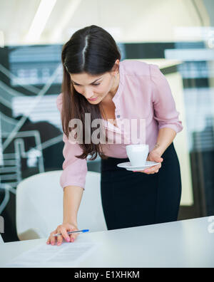 Young businesswoman reading document while holding coffee in office Stock Photo