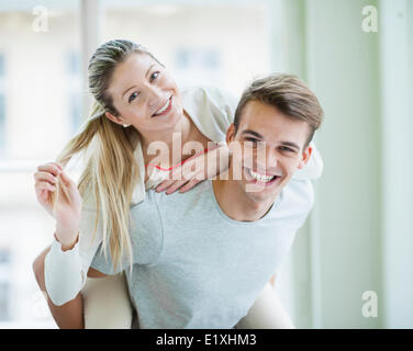 Portrait of happy young man giving piggyback ride to woman at home Stock Photo