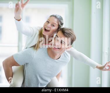 Portrait of happy woman enjoying piggyback ride given by man at home Stock Photo
