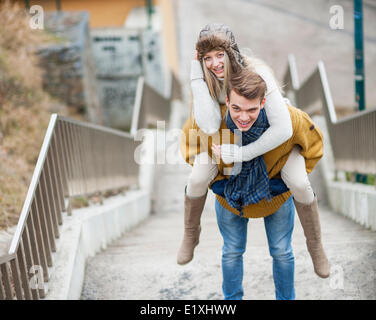 Portrait of smiling woman being piggybacked by man on stairway Stock Photo