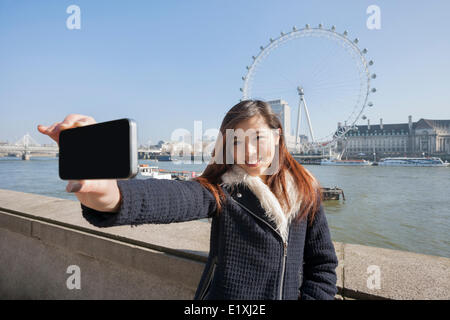 Portrait woman taking self portrait through cell phone against London Eye at London, England, UK Stock Photo