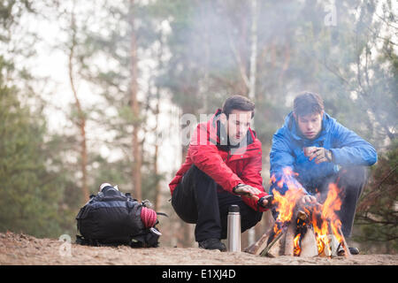 Male hikers warming hands at campfire in forest Stock Photo