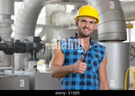 Portrait of confident young worker gesturing thumbs up in industry Stock Photo