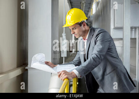 Young male architect reading blueprint while leaning on railing in industry Stock Photo