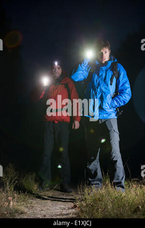 Full length portrait of male backpackers with flashlights in field at night Stock Photo