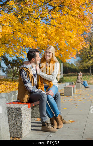 Happy woman sitting on man's lap at park during autumn Stock Photo